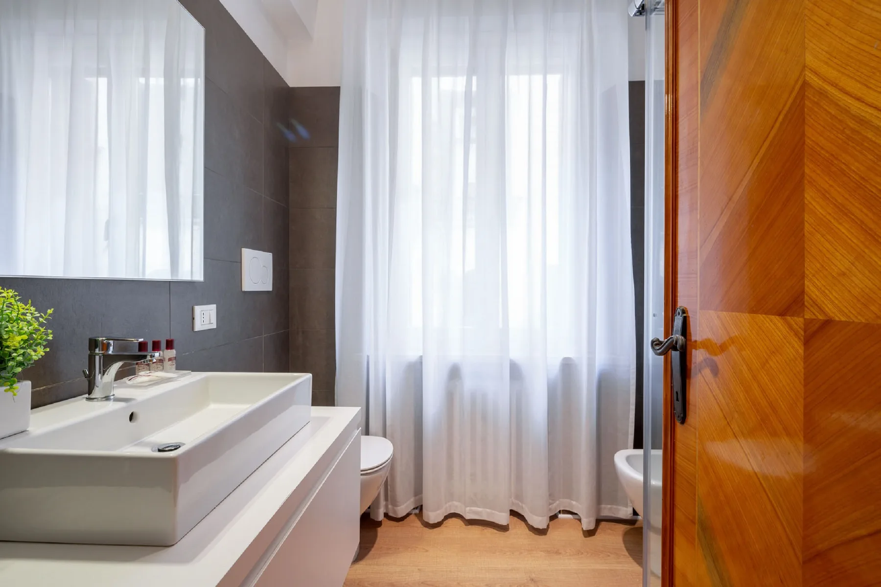 Un baño con lavabo blanco, bañera y una ventana con cortinas.