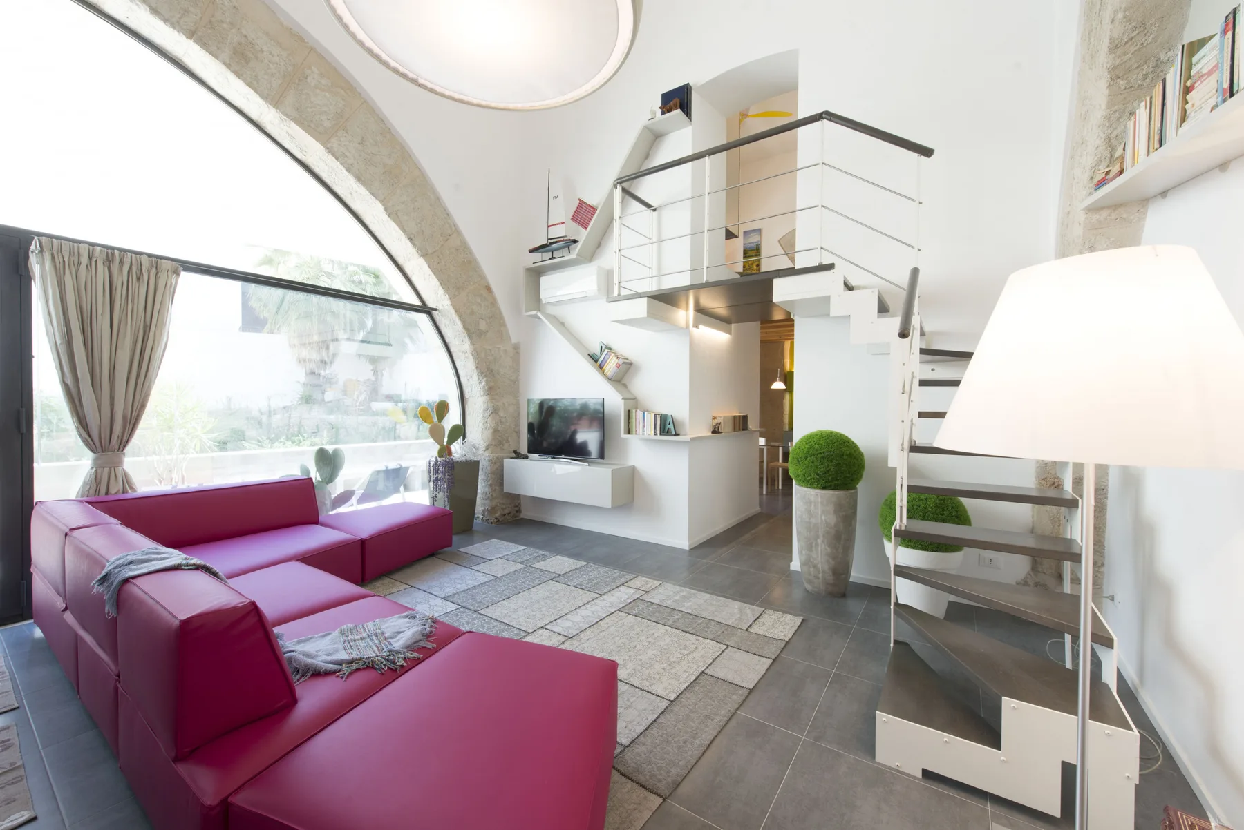 A bright living room with magenta seating beside a large arched window.