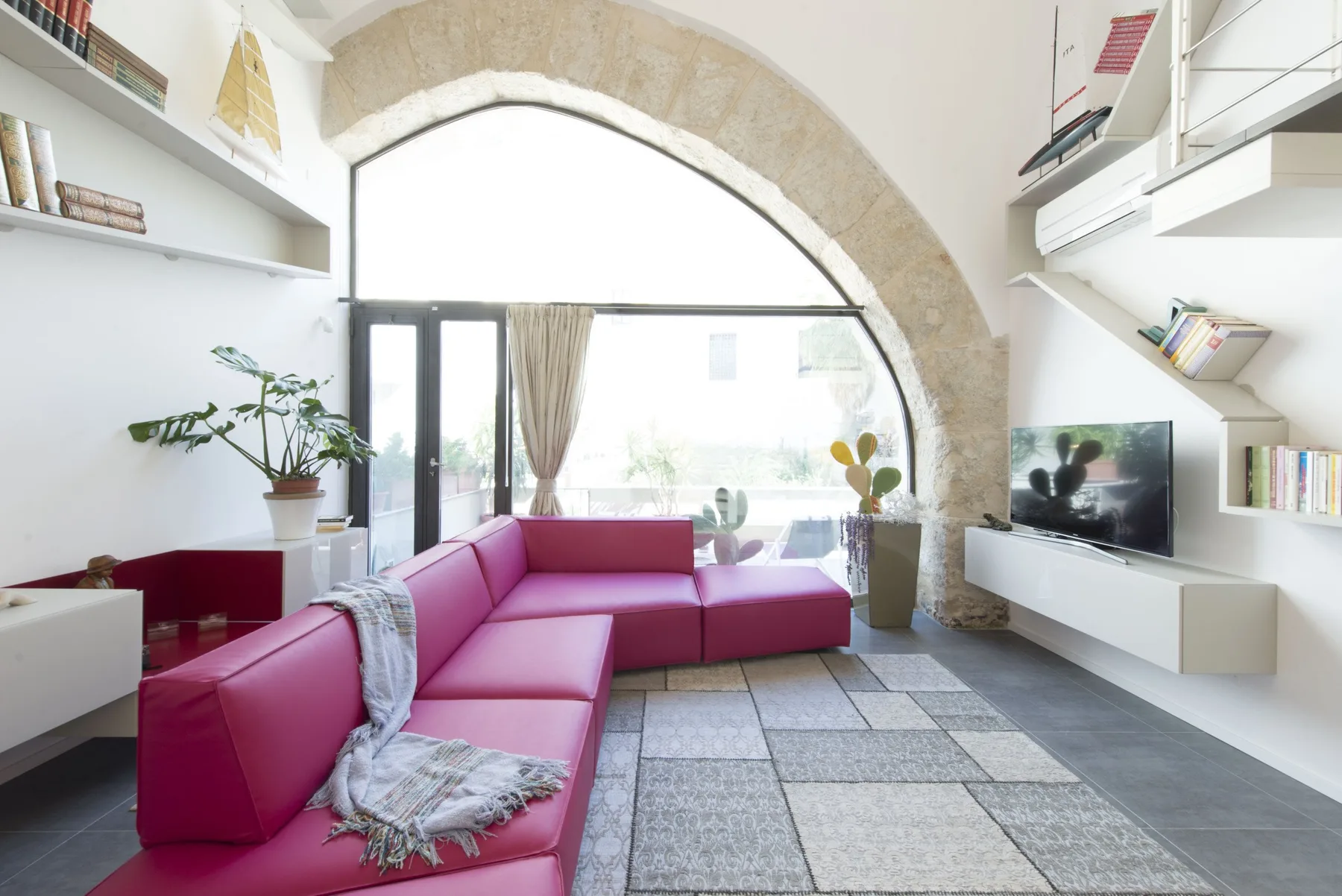 A bright living room with a magenta sectional sofa beside a large arched window.
