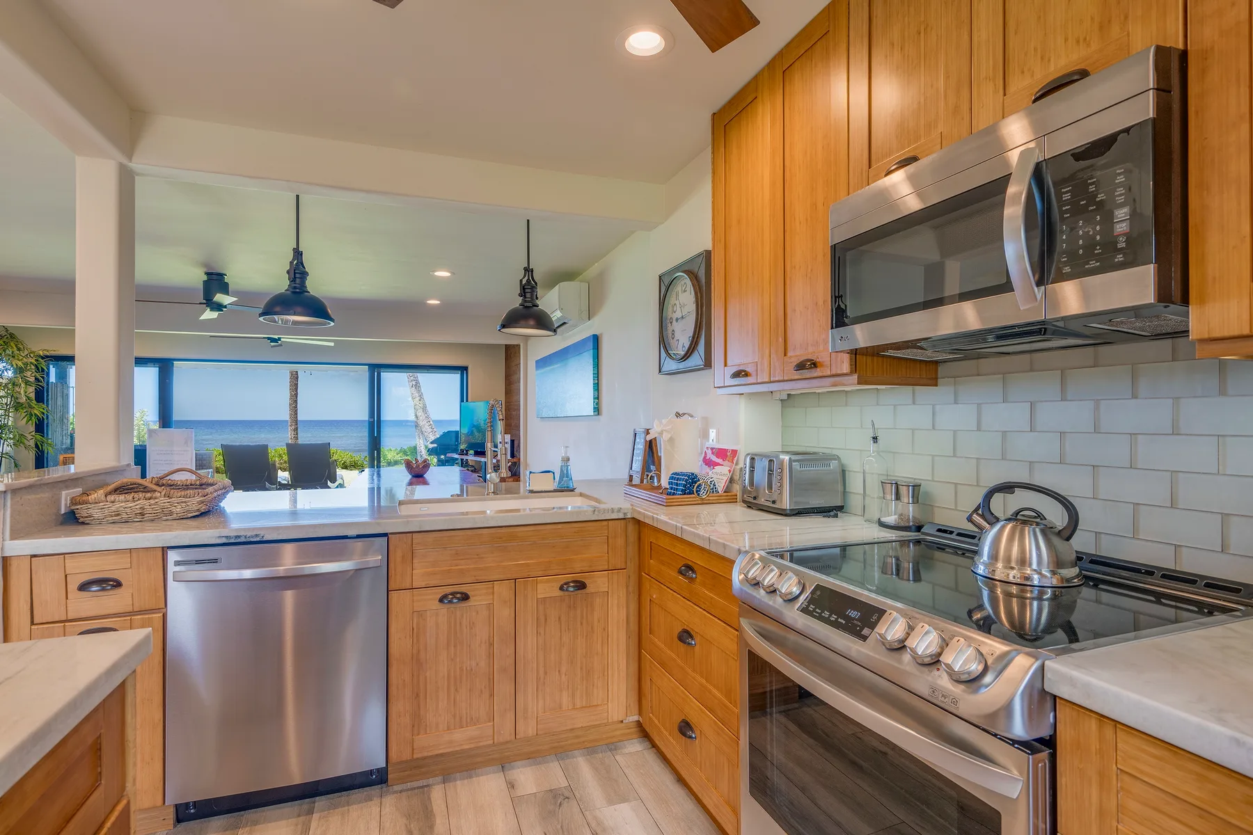 Una cocina con gabinetes de madera y electrodomésticos de acero inoxidable se abre a una sala luminosa.