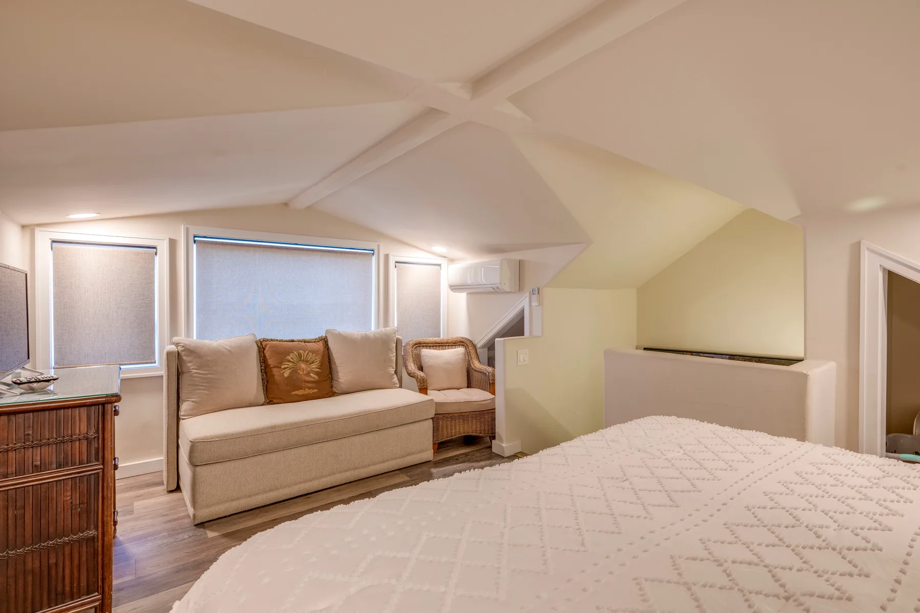 Un dormitorio con una cama y una pequeña zona de estar bajo techos inclinados.