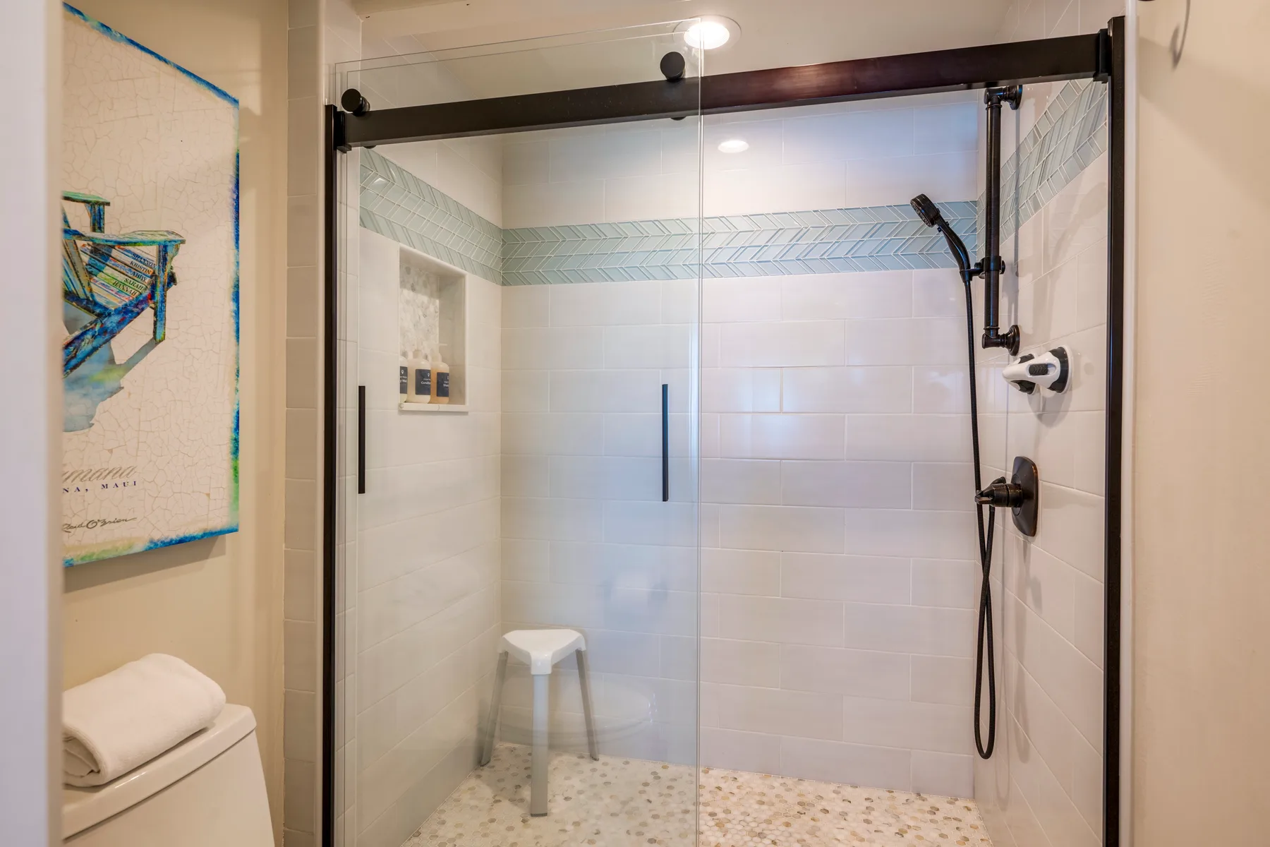Un baño con azulejos, una ducha de vidrio y un pequeño taburete.