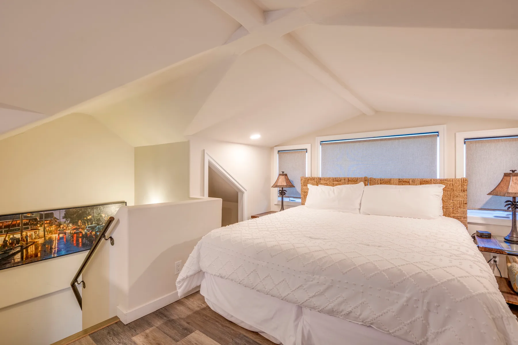 Un dormitorio con una cama grande bajo un techo inclinado y junto a varias ventanas.