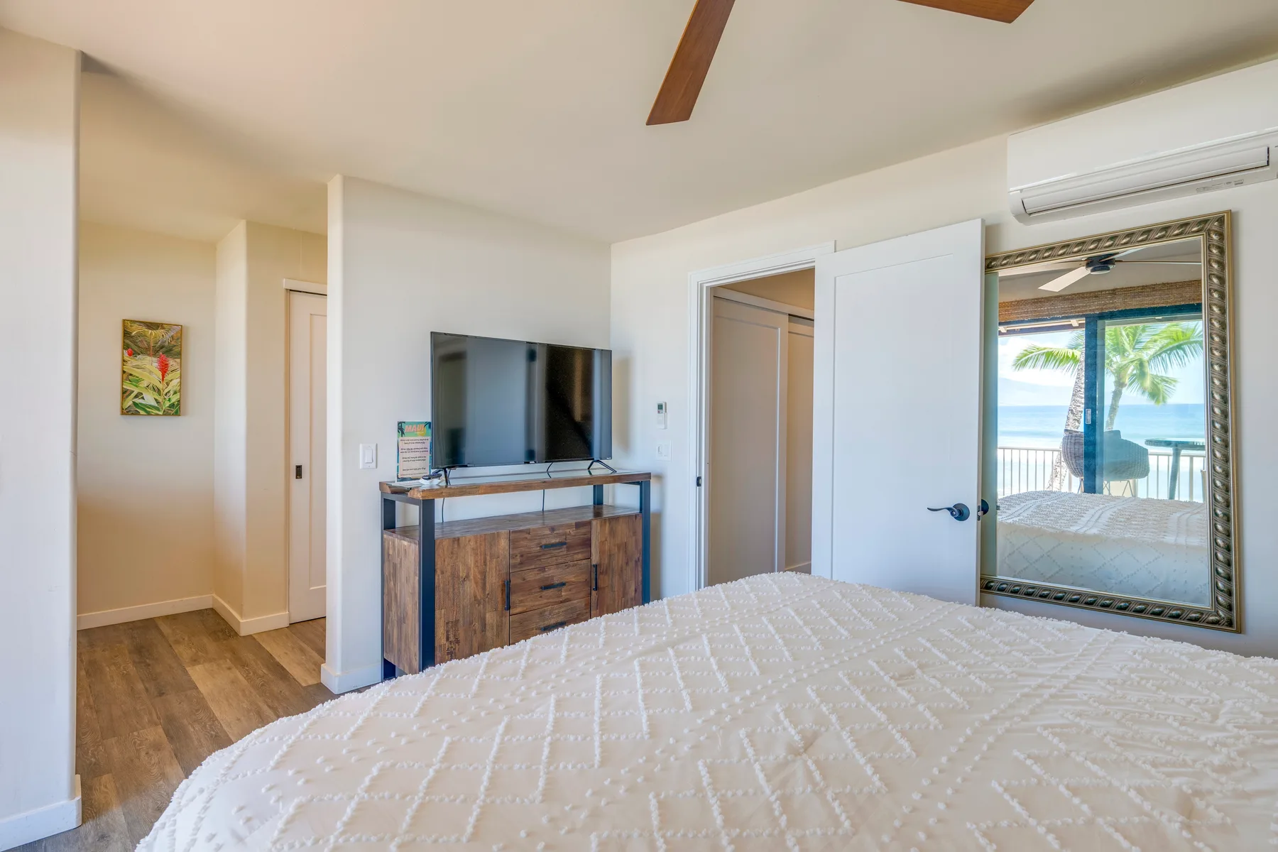 Un dormitorio con una cama, un televisor y vistas a palmeras y al océano.