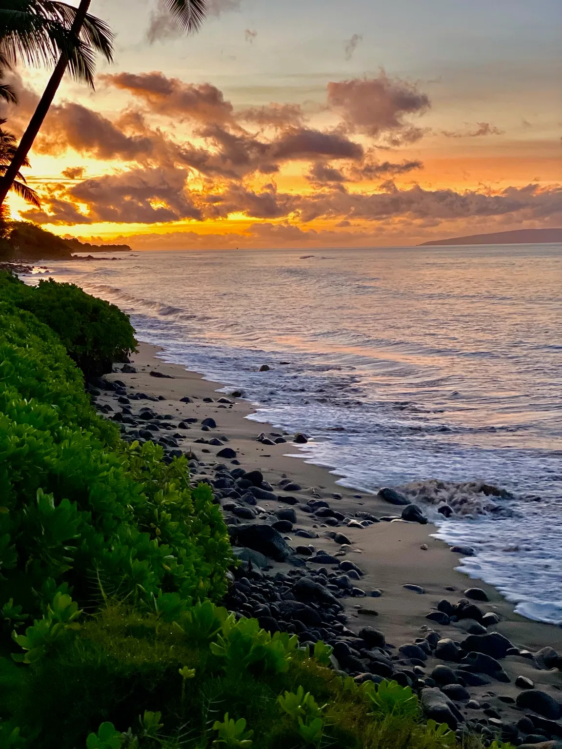Una playa tropical al atardecer, con olas que bañan una costa rocosa.