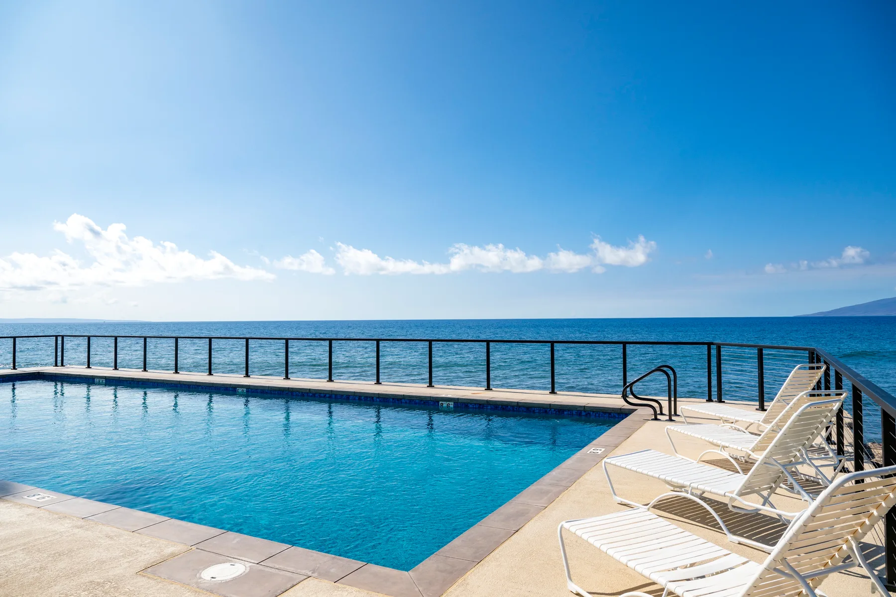 Una piscina junto al mar da al océano, con tumbonas en la terraza.