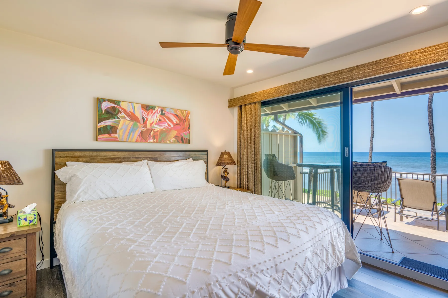 Un dormitorio con una cama grande junto a puertas corredizas de vidrio que dan a un balcón con vistas al mar.