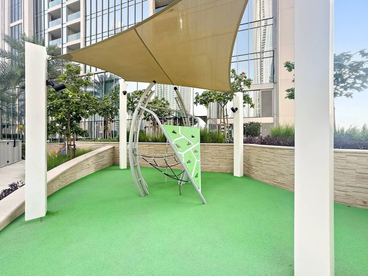A shaded outdoor play area with green flooring and climbing equipment.