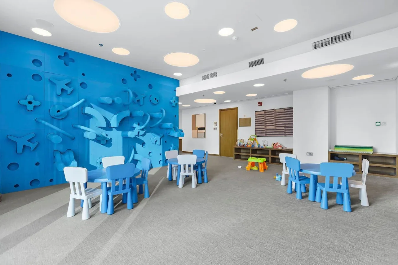 A bright children’s playroom has blue seating and a colorful wall with raised shapes.