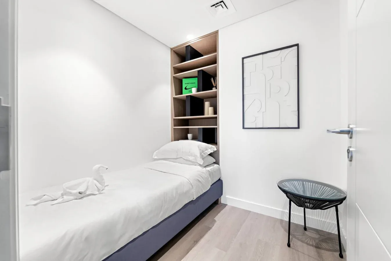 A compact bedroom with a single bed, built-in shelving, and framed wall art.