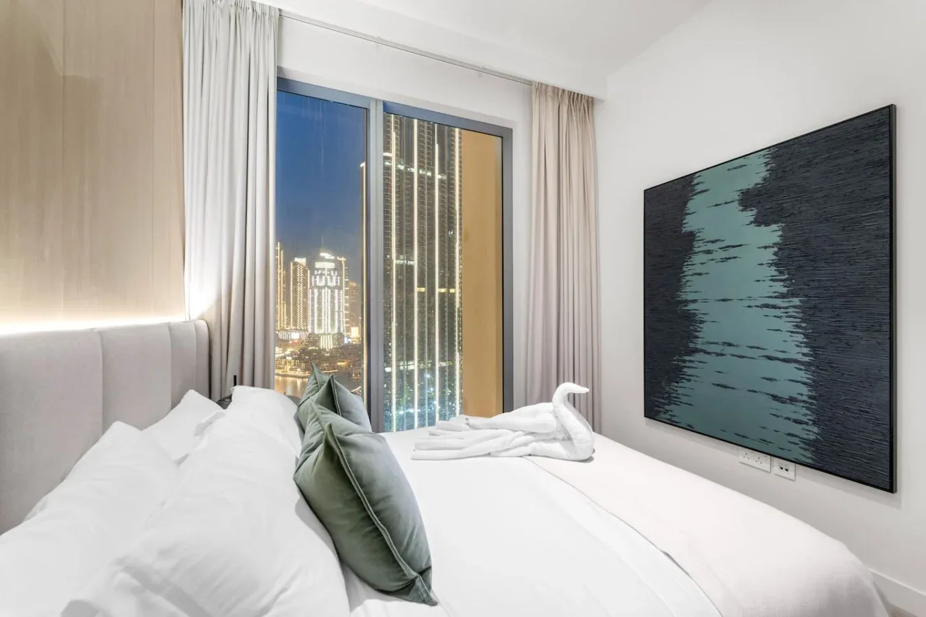 A bedroom with white bedding, a large window, and a framed abstract artwork.