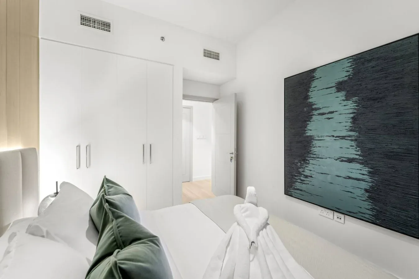 A bright bedroom with a neatly made bed and dark abstract wall art.