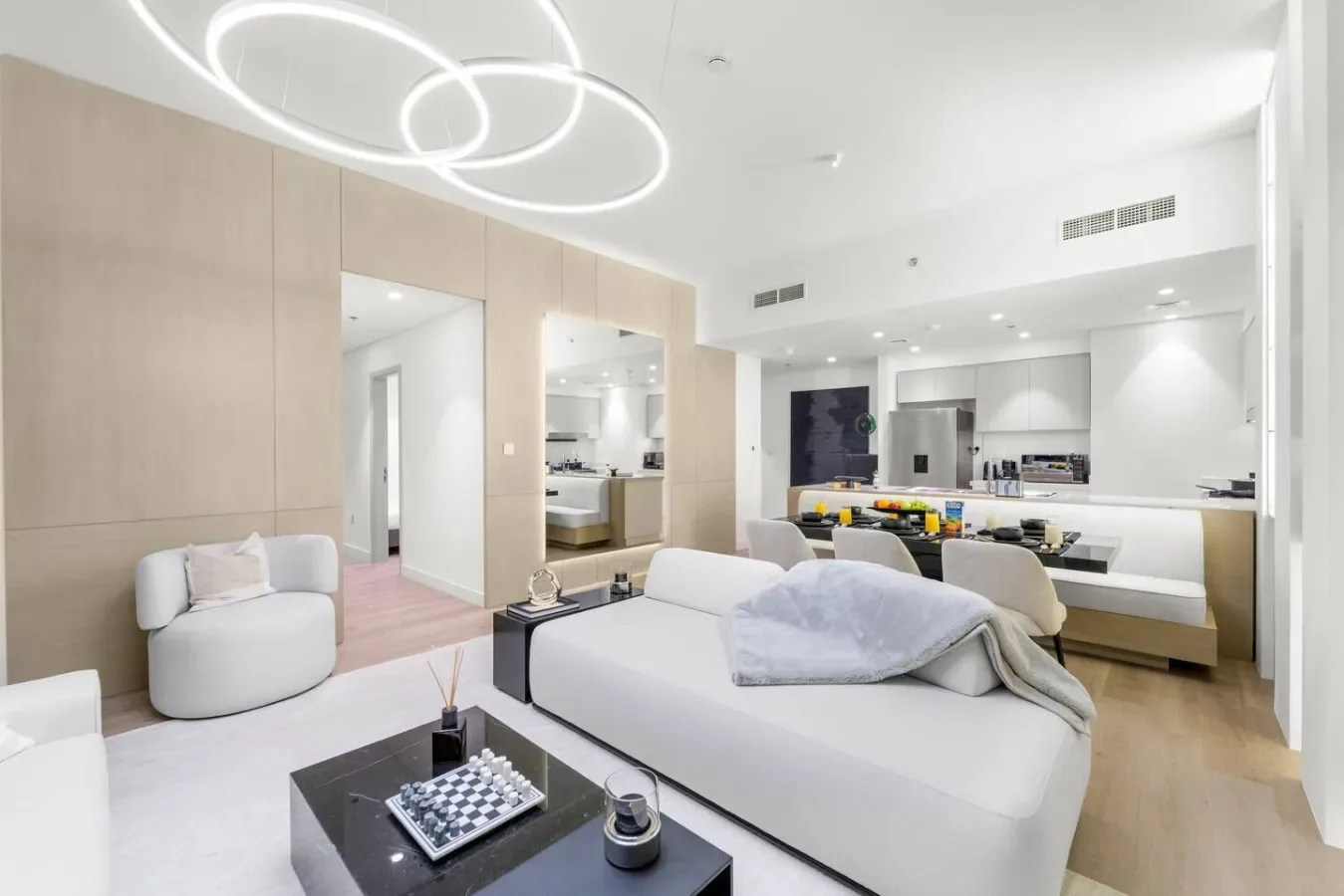 A bright bedroom with a bed and an open kitchen-dining area beyond.