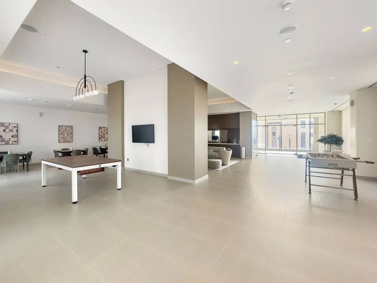 A bright shared indoor lounge with seating, a dining table, and large windows.