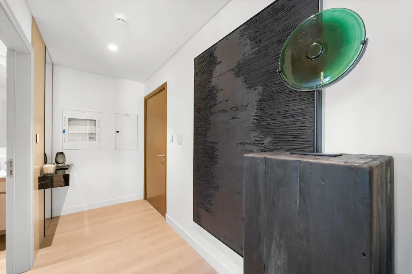 A bright hallway with a wooden door and a dark wall-mounted artwork.