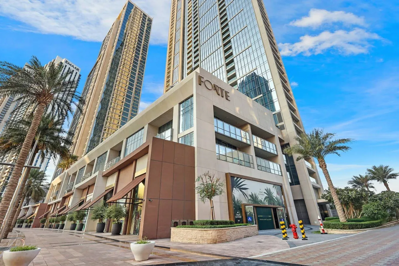 A modern high-rise building with glass windows and palm trees along the entrance.