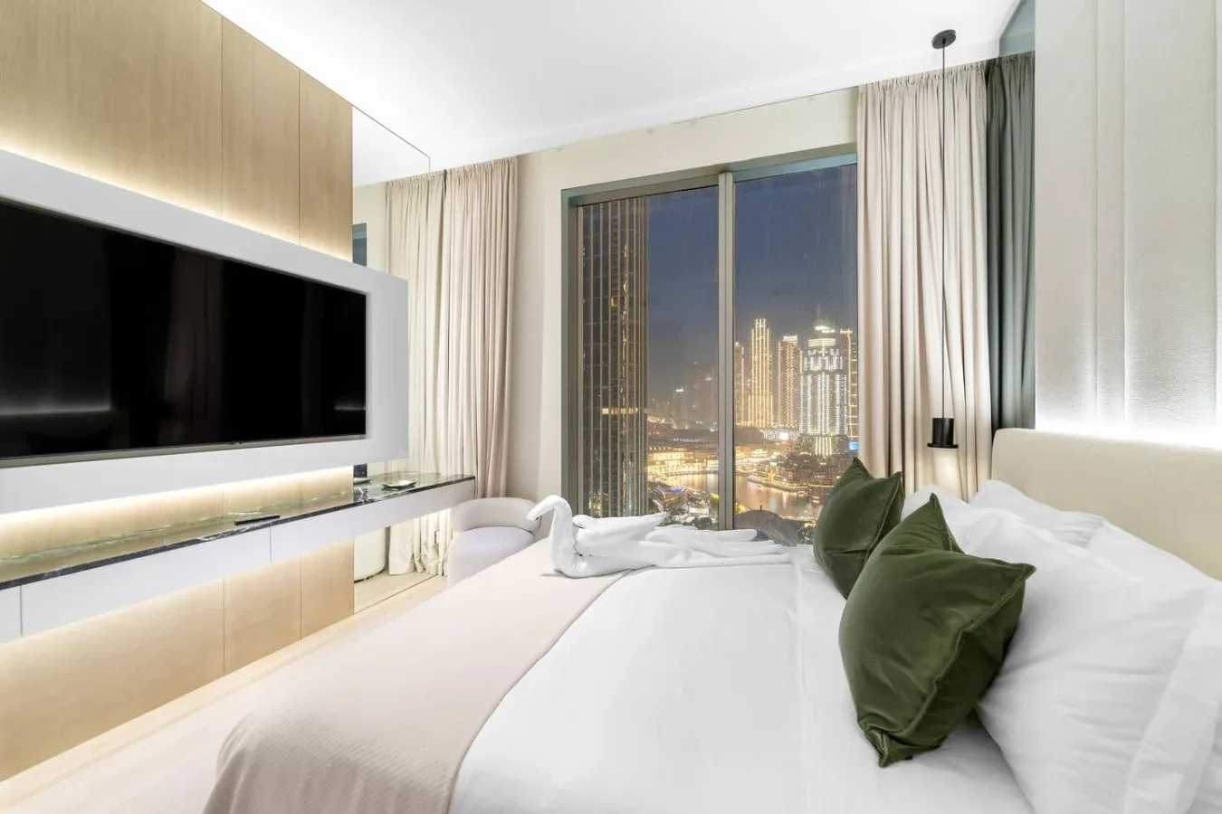 A bedroom with a large bed, green cushions, and a city view through the window.