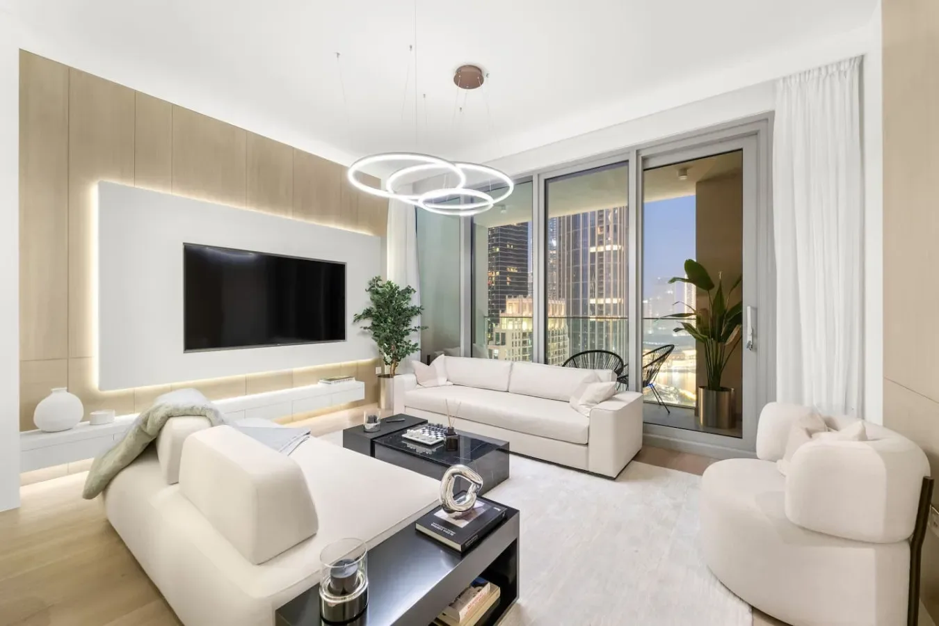A bright living room with pale seating, a television, and large windows.