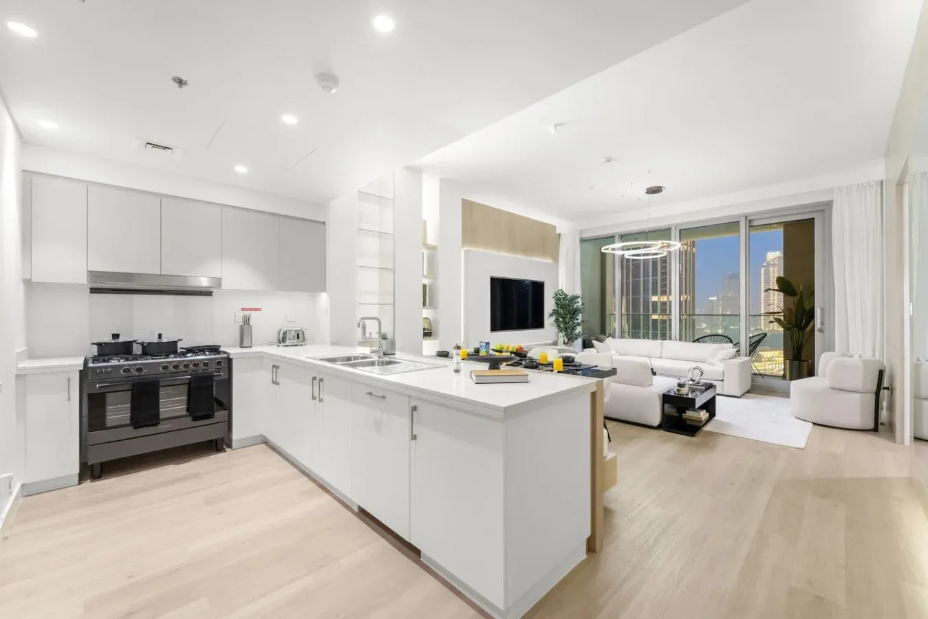 A bright open-plan kitchen and living area with white cabinetry and a seating space.