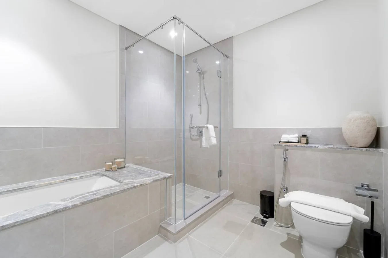 A bright bathroom with a glass shower, bathtub, and toilet.