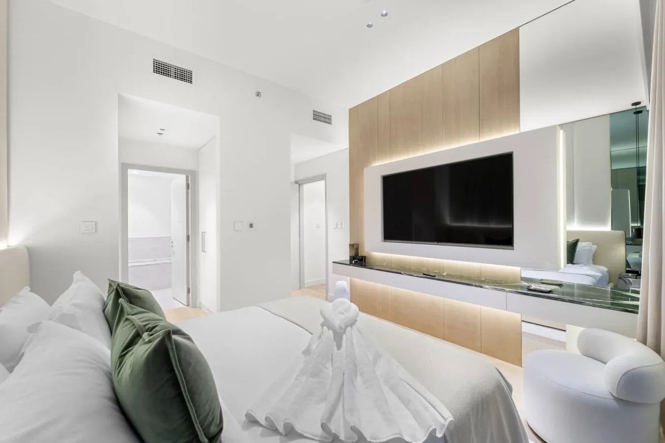 A bright bedroom with a bed facing a wall-mounted television and wood cabinetry.