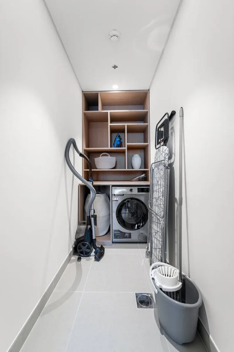 A narrow laundry room with a washer, dryer, and cleaning tools.