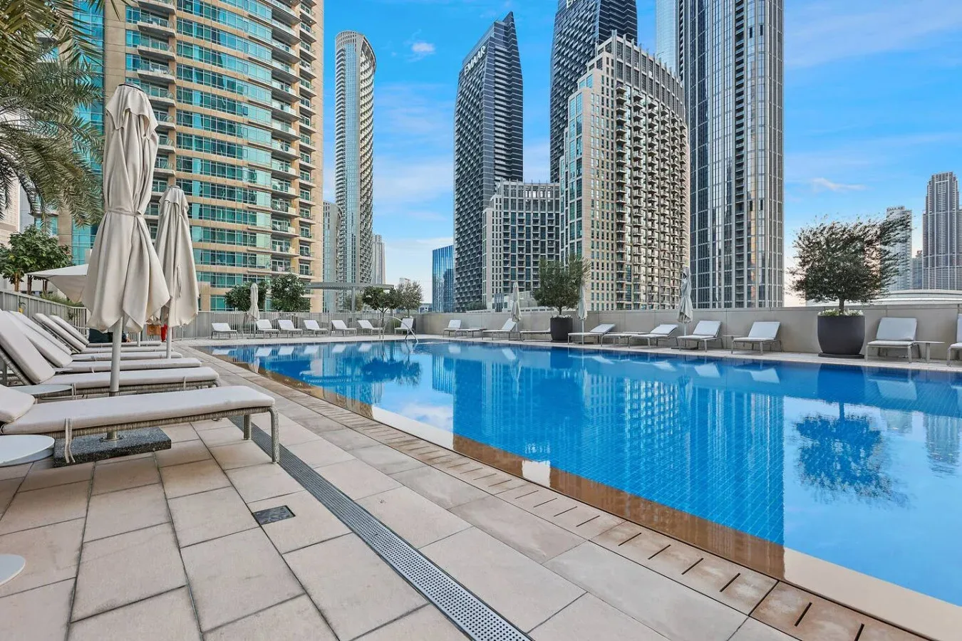 A rooftop swimming pool with lounge seating and high-rise buildings in the background.