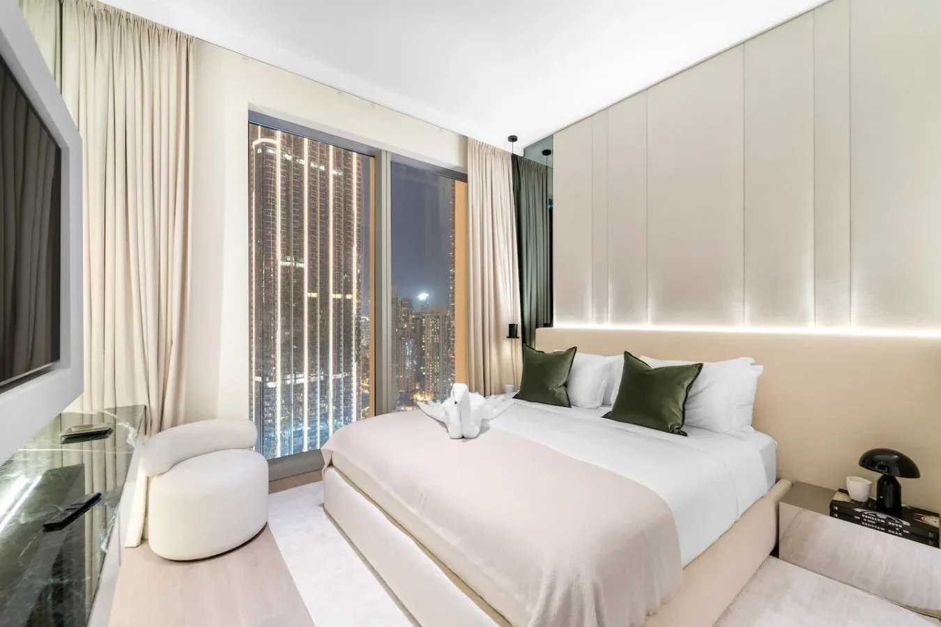 A bright bedroom with a neatly made bed and large windows overlooking city lights.