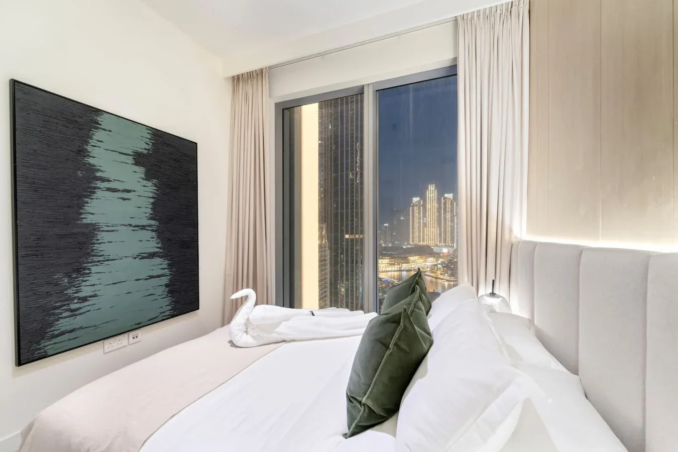 A bedroom with a neatly made bed, green cushions, and a city view through the window.