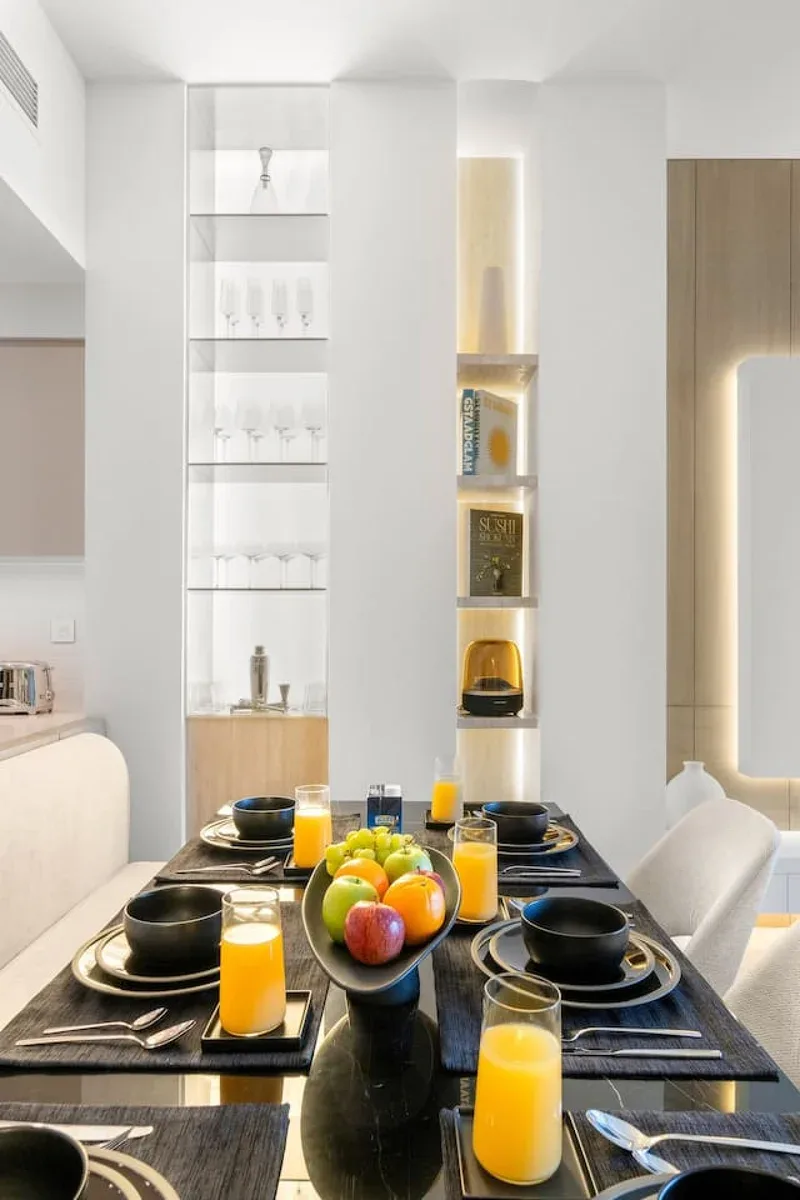 A dining table is set with plates, glasses, and a bowl of fruit.