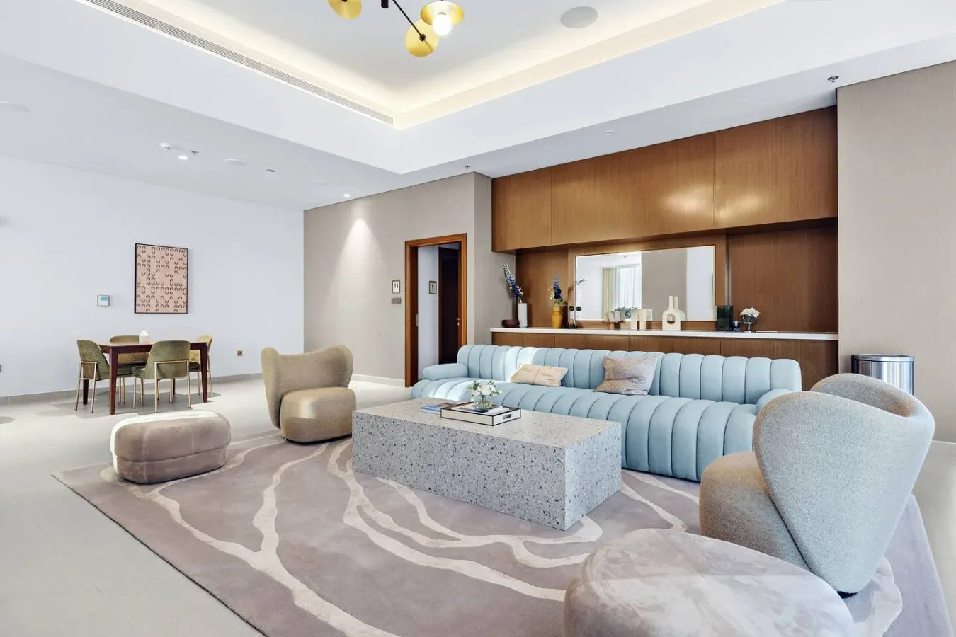 A spacious living room has blue seating, a central table, and a dining area.