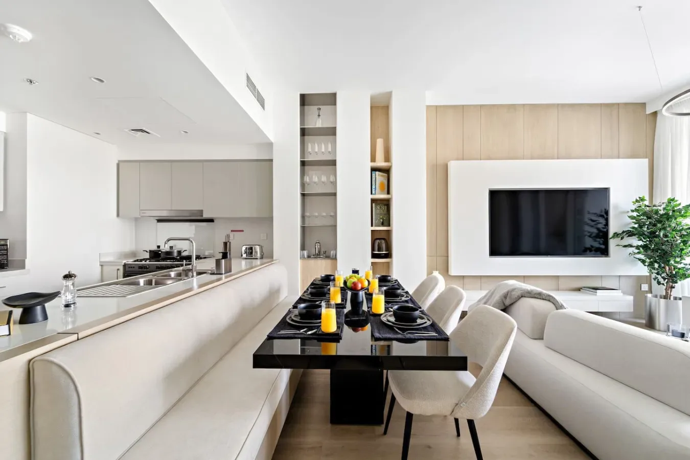 A bright open-plan living room and kitchen with a dining table between them.