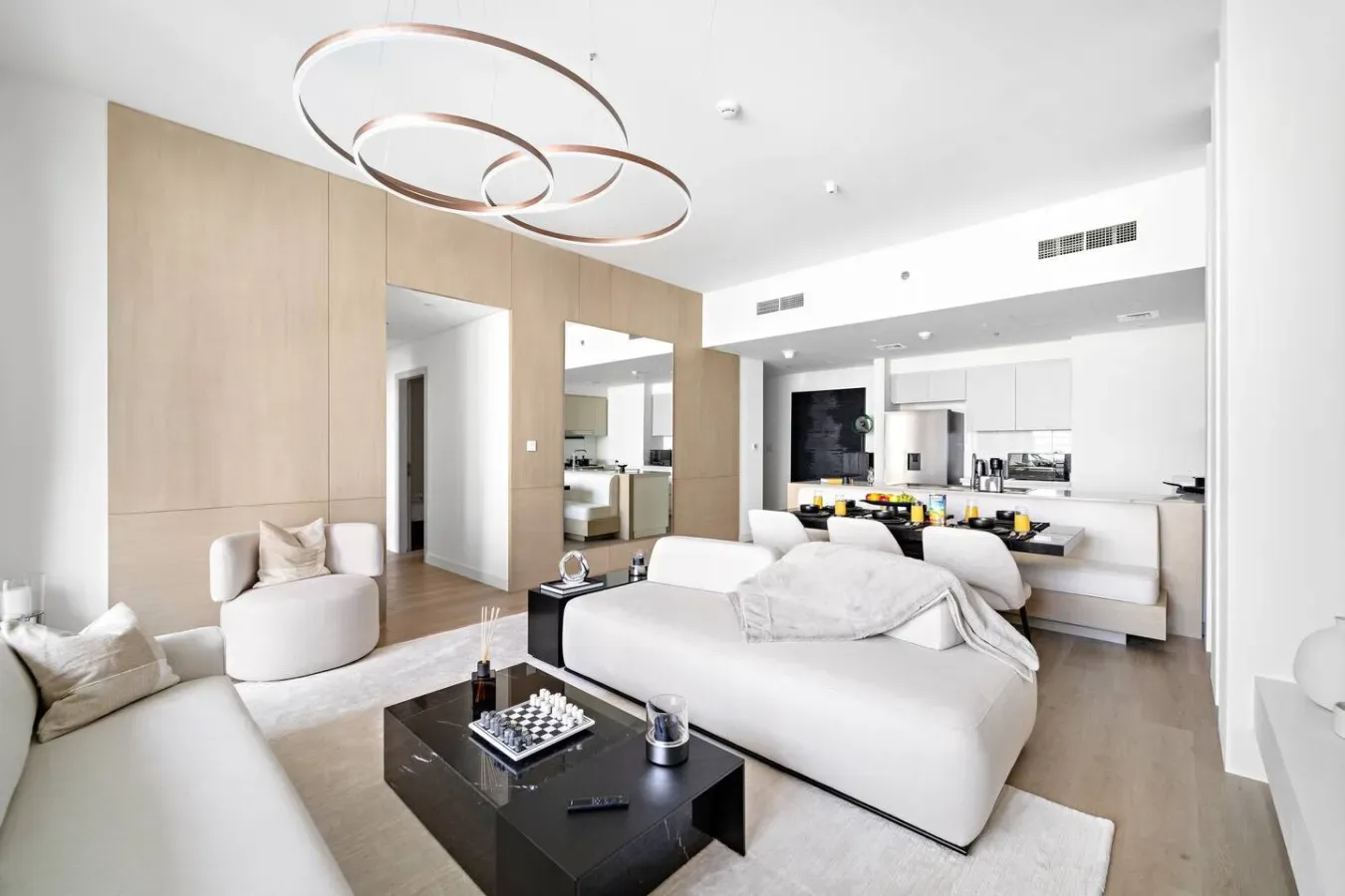 A modern open-plan living area with white seating and a kitchen behind it.
