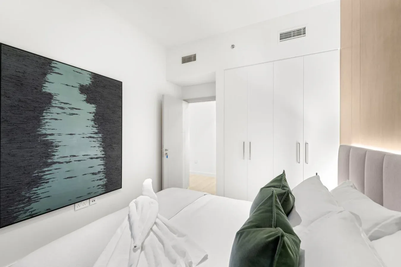 A bright bedroom with white bedding and a large abstract artwork on the wall.
