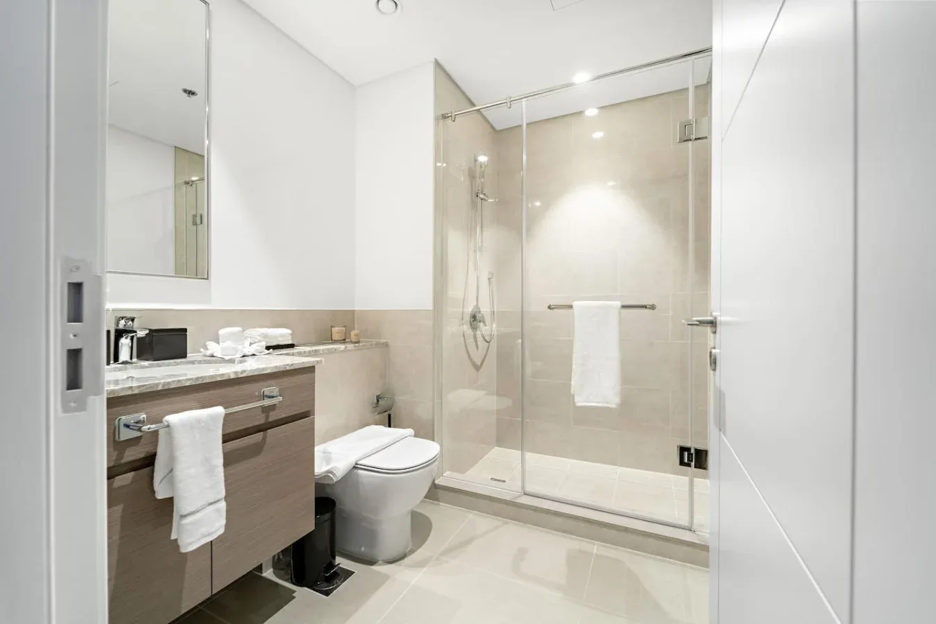 A bright bathroom with a vanity, toilet, and glass shower.
