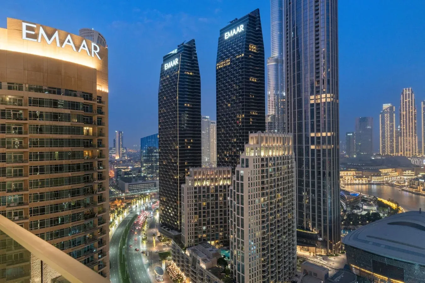 A city skyline at dusk with illuminated high-rise buildings and roads below.
