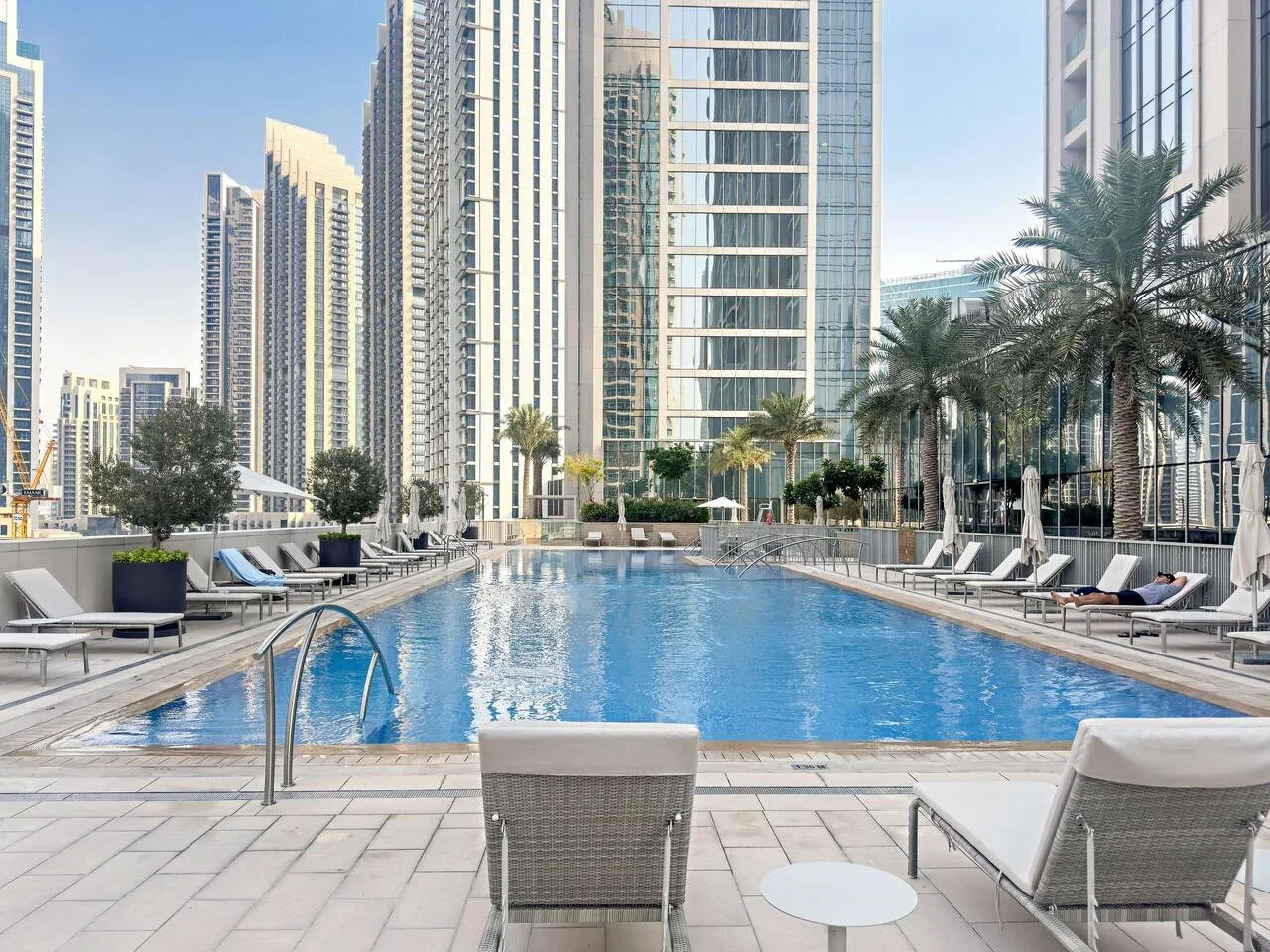 An outdoor swimming pool is surrounded by loungers and tall buildings.