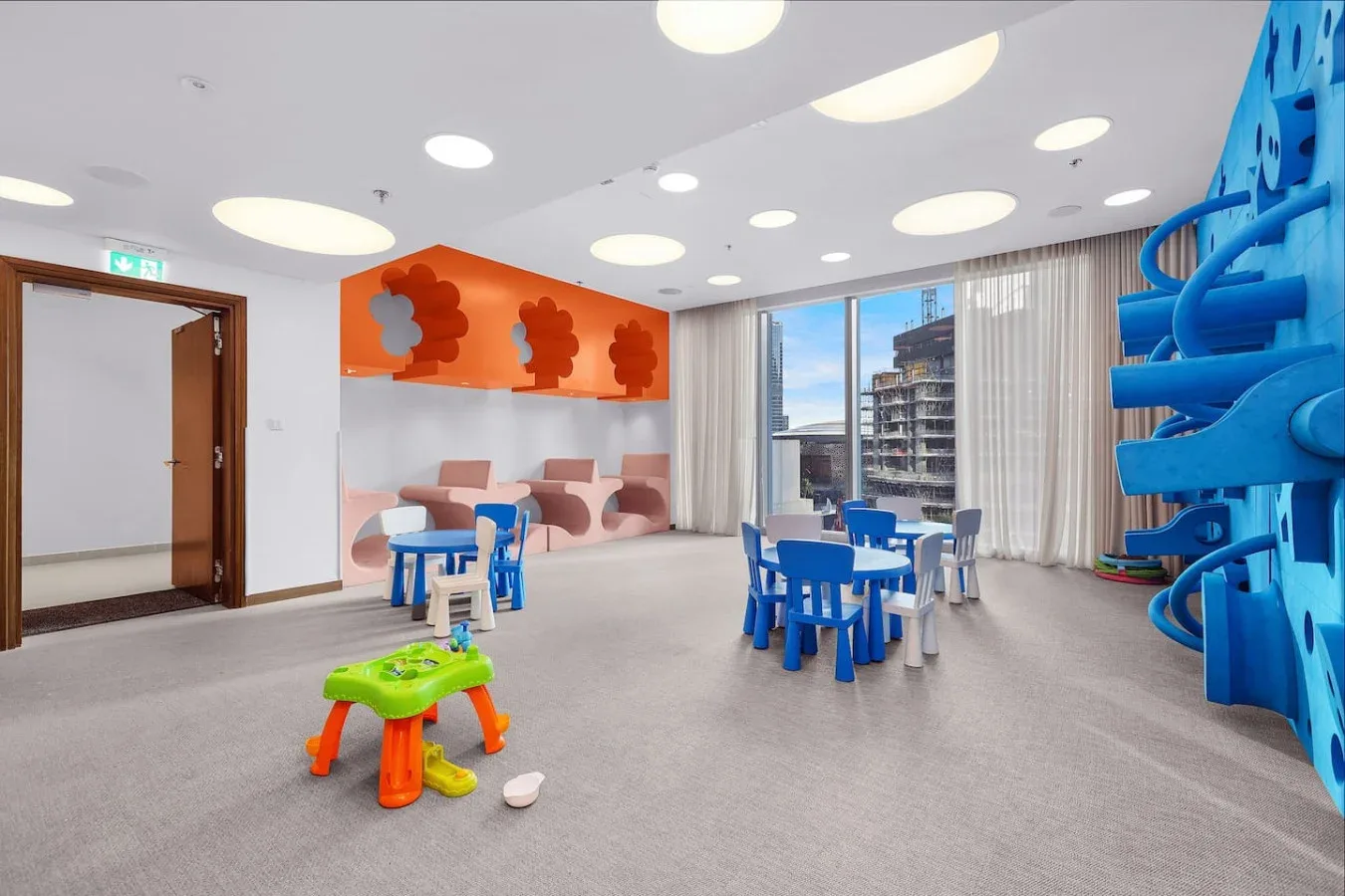 A bright indoor playroom with small tables and colorful play equipment.