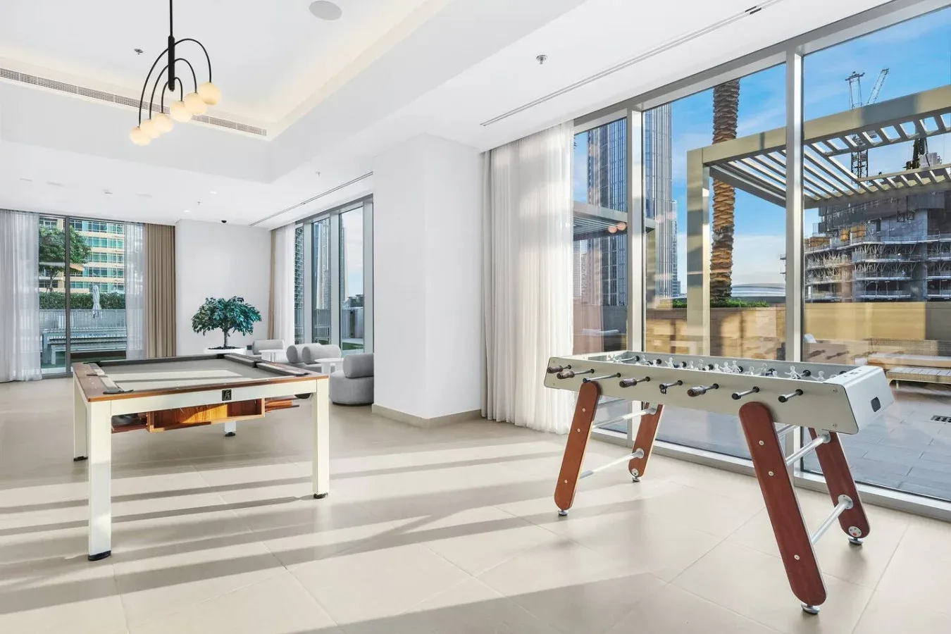 A bright recreation room with a pool table and a foosball table beside large windows.