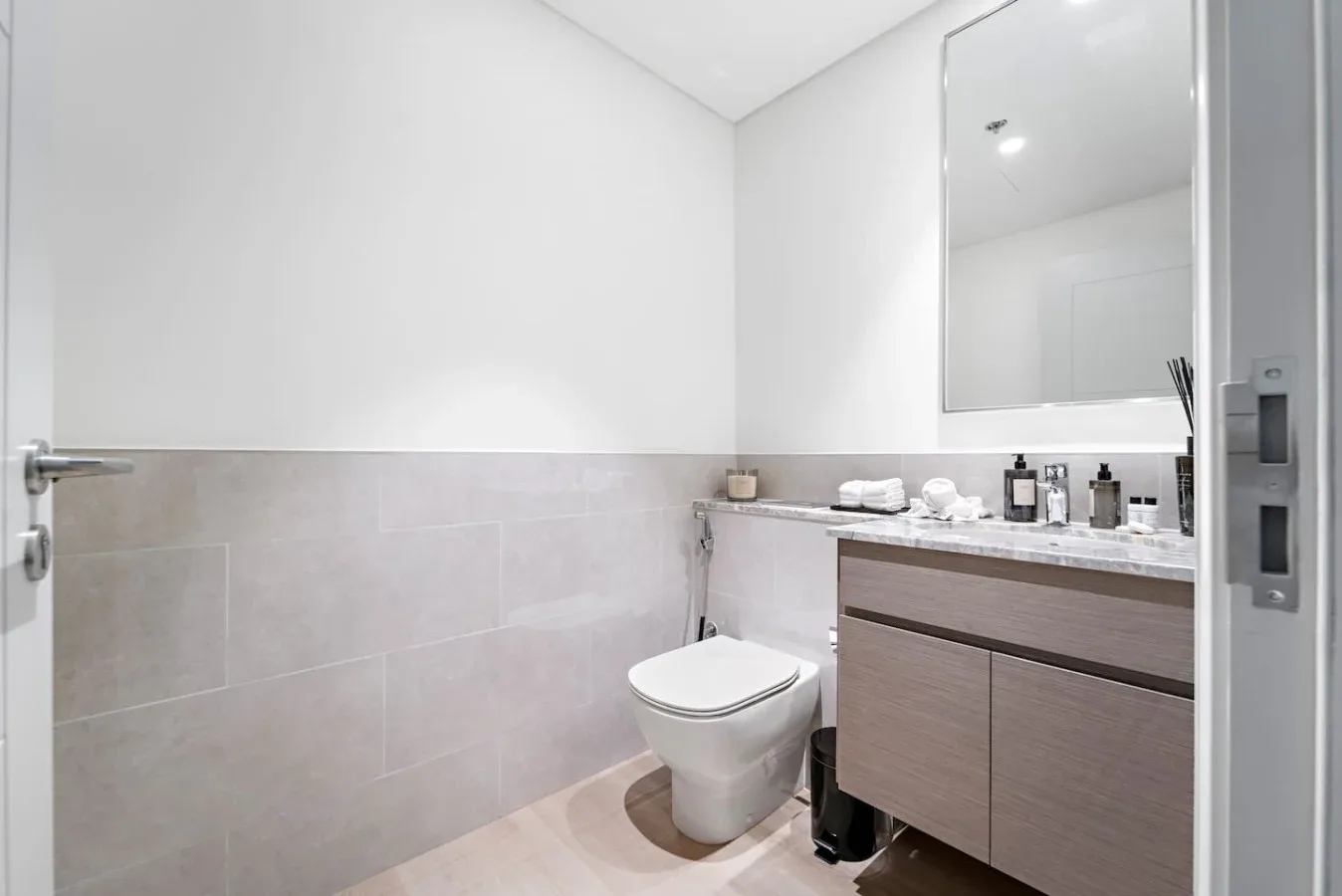 A bright bathroom with a toilet, vanity, and large wall mirror.