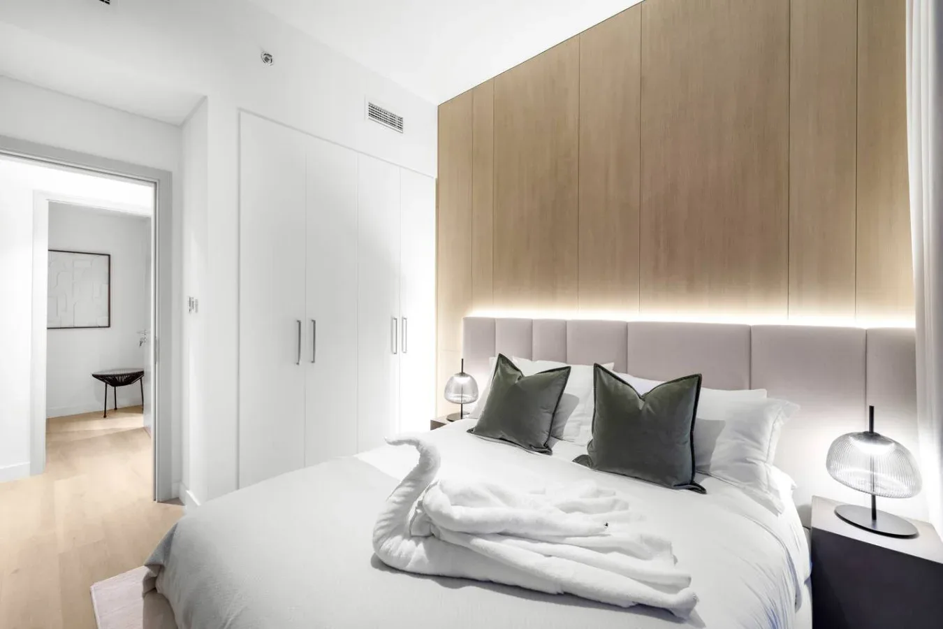 A bright bedroom with a neatly made bed beneath wood-toned wall panels.