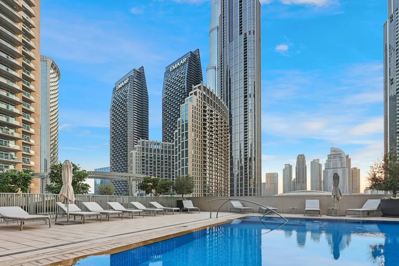 A rooftop swimming pool and lounge area overlook a cluster of city high-rises.