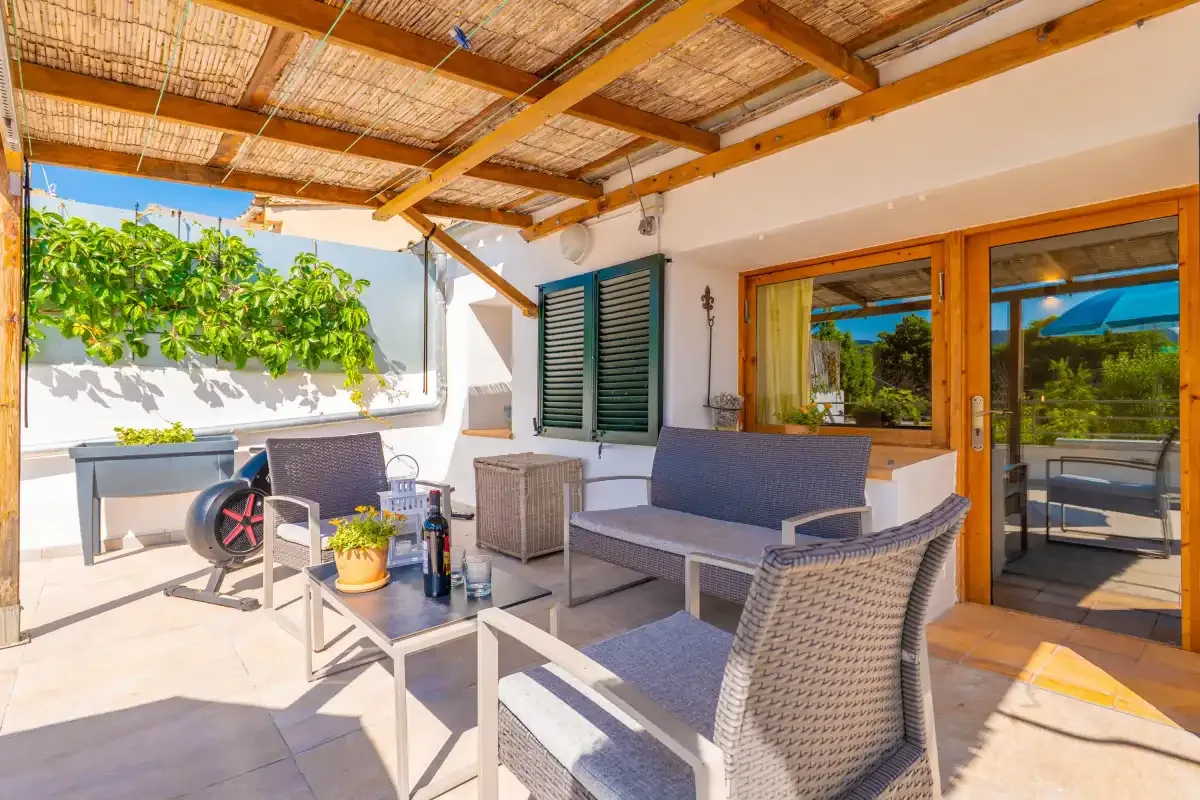 Un patio cubierto tiene asientos de mimbre, una mesa baja y puertas de vidrio.