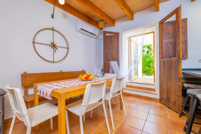 Comedor con mesa de madera, sillas blancas y puertas abiertas hacia un jardín.