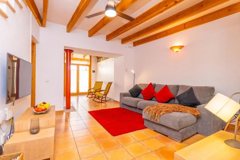 Una sala de estar con asientos grises, una alfombra roja y vigas de madera a la vista.