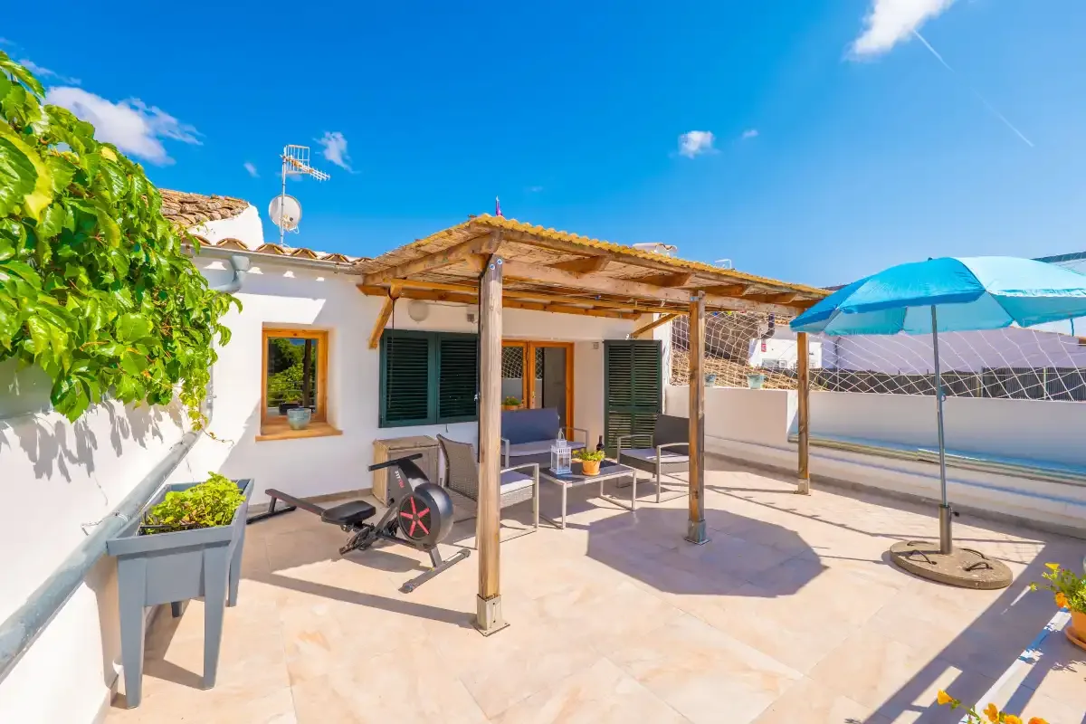Un patio soleado con asientos, una pérgola de madera y una sombrilla azul.