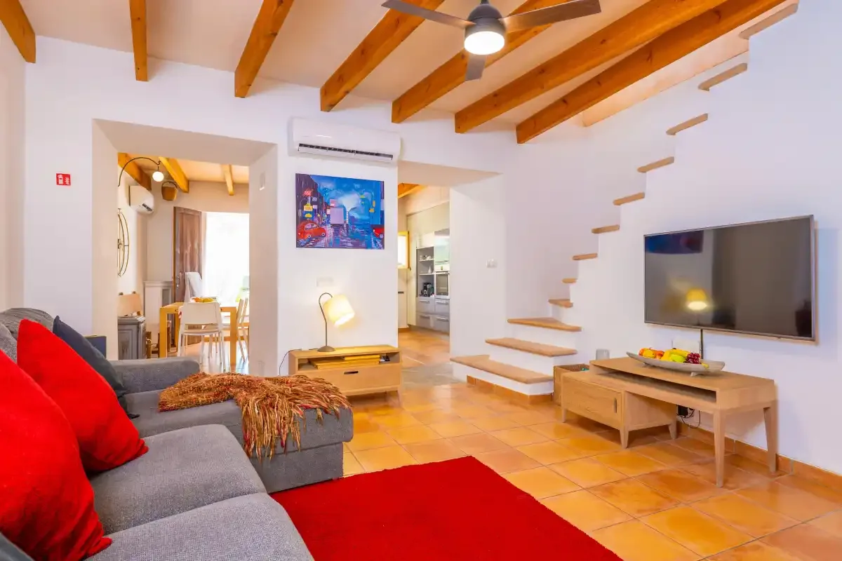 Sala de estar con asientos, un televisor y vigas de madera vistas en el techo.