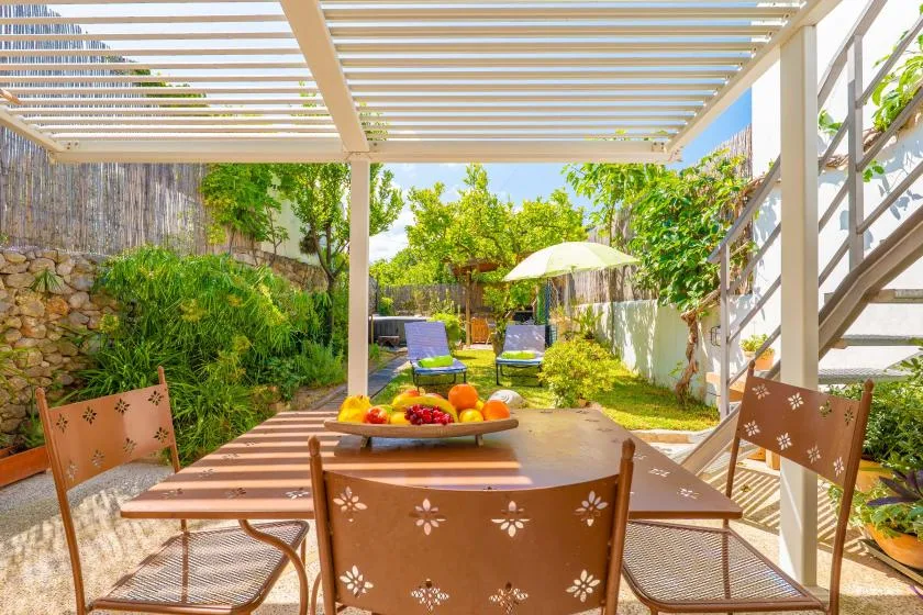 Un comedor exterior a la sombra, con mesa y sillas bajo una pérgola.