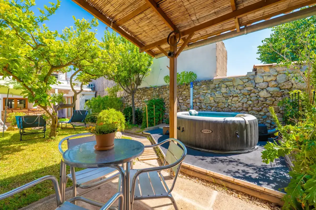 Un patio ajardinado con asientos al aire libre y una bañera de hidromasaje bajo una pérgola.