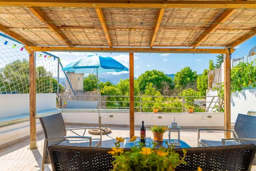 Una zona de estar al aire libre y cubierta mira hacia la vegetación, con una mesa y plantas en macetas.